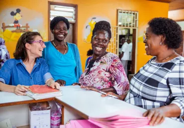 Four women laugh together at a desk in a clinic in Uganda.