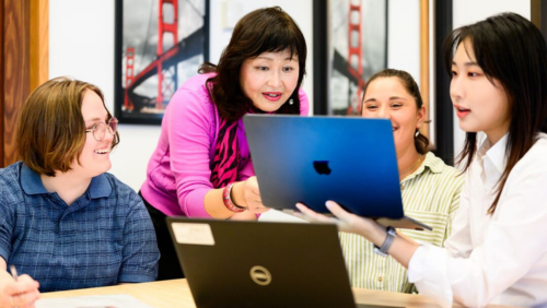 Instructor and three students looking at a laptop screen.