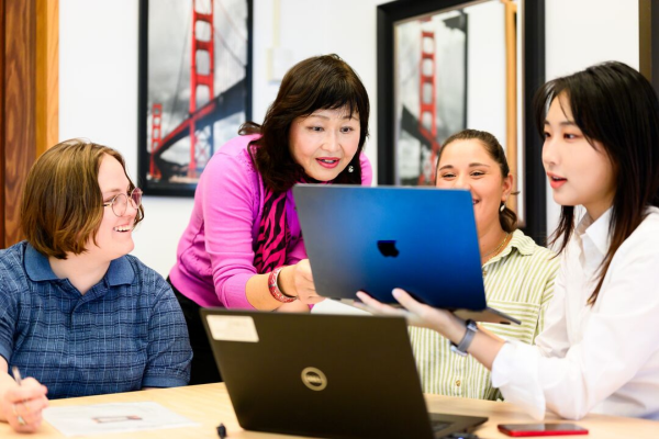 Instructor and three students looking at a laptop screen.