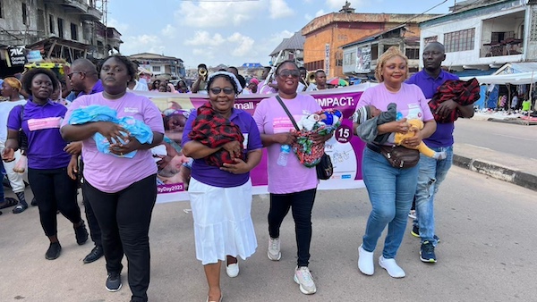 Four GAIN staff wearing purple and holding infants while marching in a parade. 