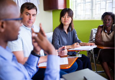 Three people listening to a speaker in a classroom in Uganda.