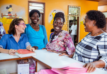 Four women laugh together at a desk in a clinic in Uganda. 